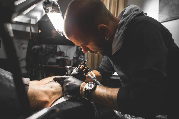 Le tatoueur crée une image sur le corps d'un homme. gros plan des machines à tatouer et des mains — Photo