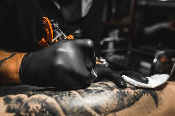 The tattoo artist creates a picture on the body of a man. close-up of tattoo machines and hands