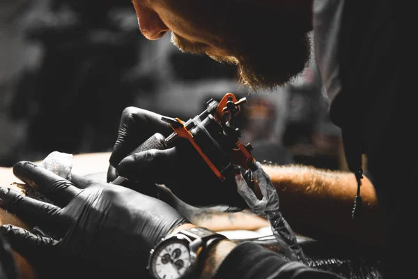 O tatuador cria uma imagem no corpo de um homem. close-up de máquinas de tatuagem e mãos — Fotografia de Stock