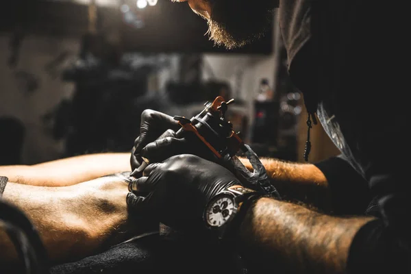 Le tatoueur crée une image sur le corps d'un homme. gros plan des machines à tatouer et des mains — Photo
