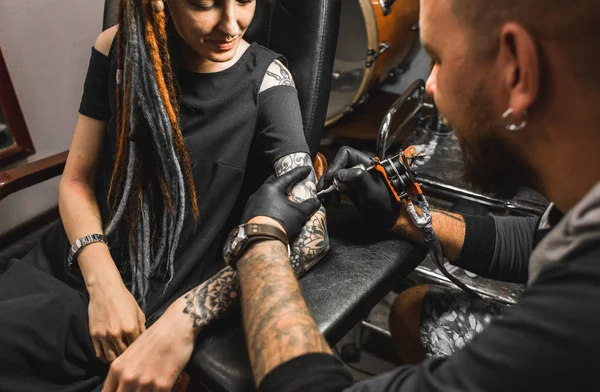 Fille avec dreadlocks dans un salon de tatouage. Le maître crée une image sur le corps d'une jeune belle fille. Gros plan des mains et de la machine à tatouer — Photo