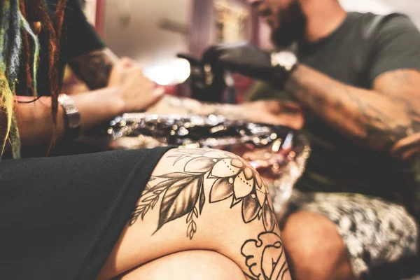 Дівчина з дредлоками в татуювальному салоні. Майстер створює зображення на тілі молодої красивої дівчини. Крупним планом руки і татуювання машини — стокове фото