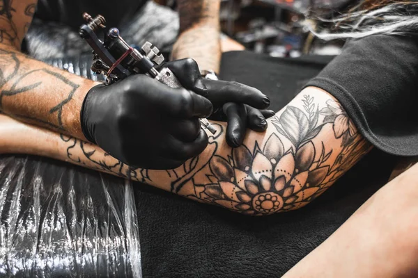 Girl with dreadlocks in a tattoo parlor. The master creates a picture on the body of a young beautiful girl. Close-up of hands and tattoo machine — Stock Photo, Image