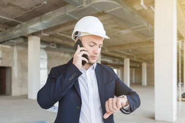 Erkek mühendis, Foreman'ın kağıt çizim, tamamlanmakta inşaat ile iş elbiseli bir kask içinde cep telefonu üzerinde konuşurken. Yapı Denetim