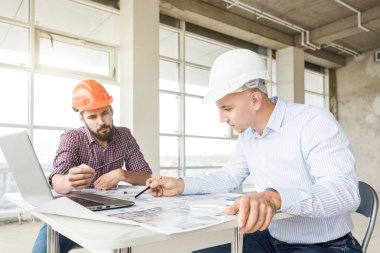Erkek mühendisler, mimarlar kask masasında çalışıyor. Çizimler, dizüstü bilgisayar, masaüstü rulet. Resepsiyon ve inşaat yapı denetim