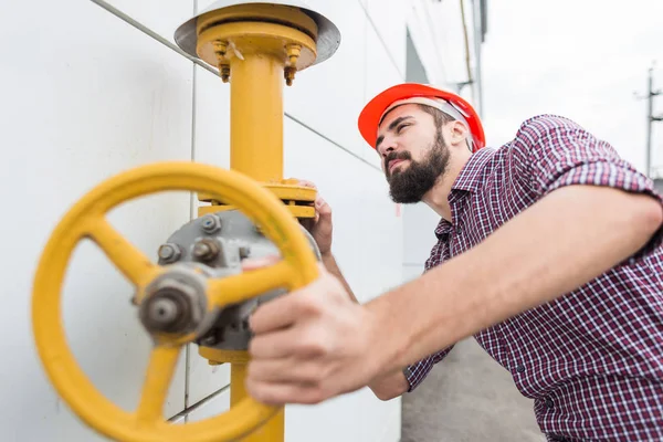 Trabajador de la central eléctrica. hombre ingeniero en casco y camisa tuerce válvula de tubería de gas — Foto de Stock