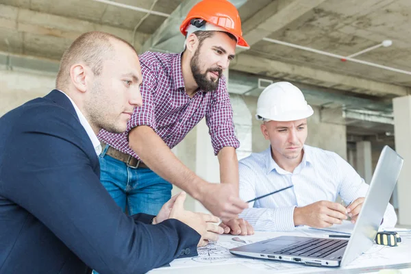 male engineers, architects working at the desk in helmets. Drawings, laptop, roulette on the desktop. Reception and supervision of building construction