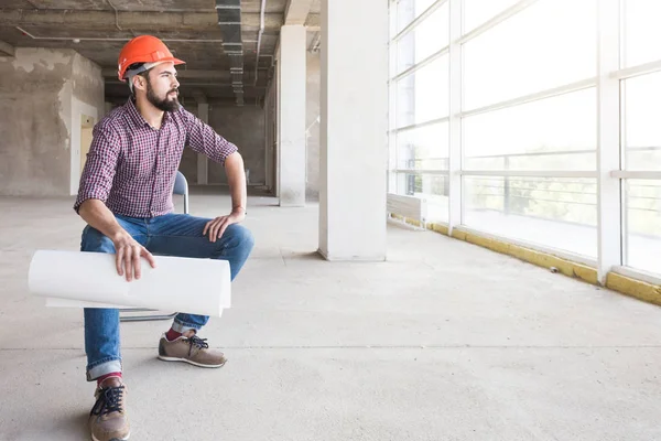 the man is an engineer in a helmet, in a checkered shirt with paper with drawings, in the construction being completed. building supervision