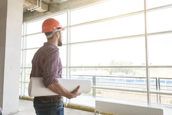 the man is an engineer in a helmet, in a checkered shirt with paper with drawings, in the construction being completed. building supervision