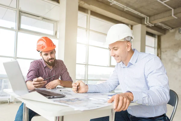 male engineers, architects working at the desk in helmets. Drawings, laptop, roulette on the desktop. Reception and supervision of building construction