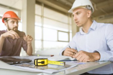 Erkek mühendisler, mimarlar kask masasında çalışıyor. Çizimler, dizüstü bilgisayar, masaüstü rulet. Resepsiyon ve inşaat yapı denetim