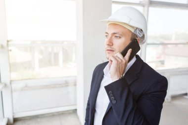 Erkek mühendis, Foreman'ın kağıt çizim, tamamlanmakta inşaat ile iş elbiseli bir kask içinde cep telefonu üzerinde konuşurken. Yapı Denetim