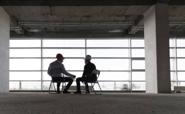 Erkek mühendisler tablo ile bir dizüstü bilgisayar, iş görüşmeleri inşaat alanındaki çalışma yapanlar. siluetleri pencerenin arka planı