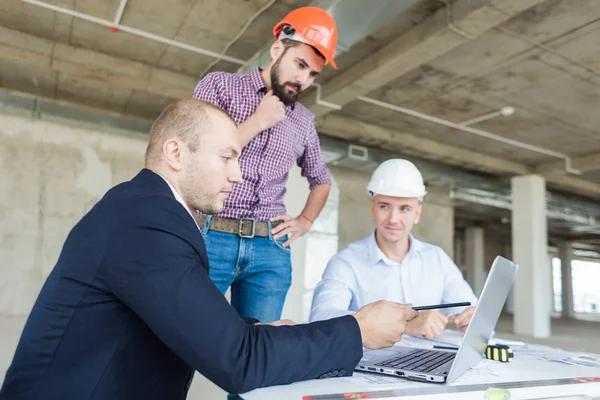 male engineers, architects working at the desk in helmets. Drawings, laptop, roulette on the desktop. Reception and supervision of building construction