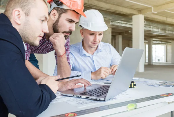 male engineers, architects working at the desk in helmets. Drawings, laptop, roulette on the desktop. Reception and supervision of building construction