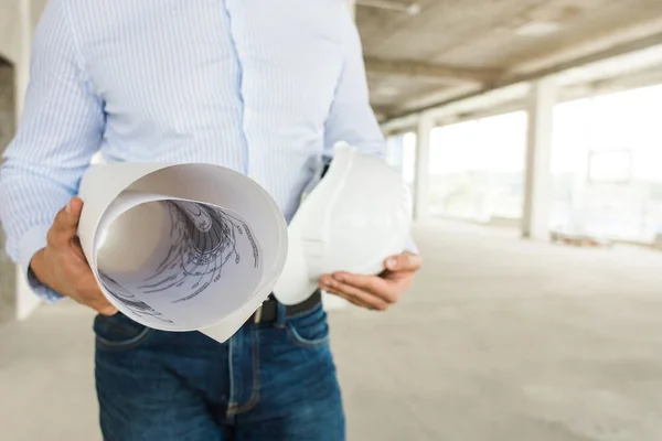 Ingeniero masculino, arquitecto en casco en la obra sostiene dibujo sobre papel en las manos — Foto de Stock