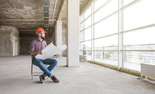 the man is an engineer in a helmet, in a checkered shirt with paper with drawings, in the construction being completed. building supervision