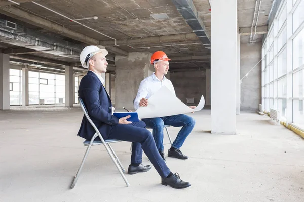 Hombres ingenieros constructores que trabajan en la mesa con un ordenador portátil, negociaciones comerciales en el sitio de construcción — Foto de Stock