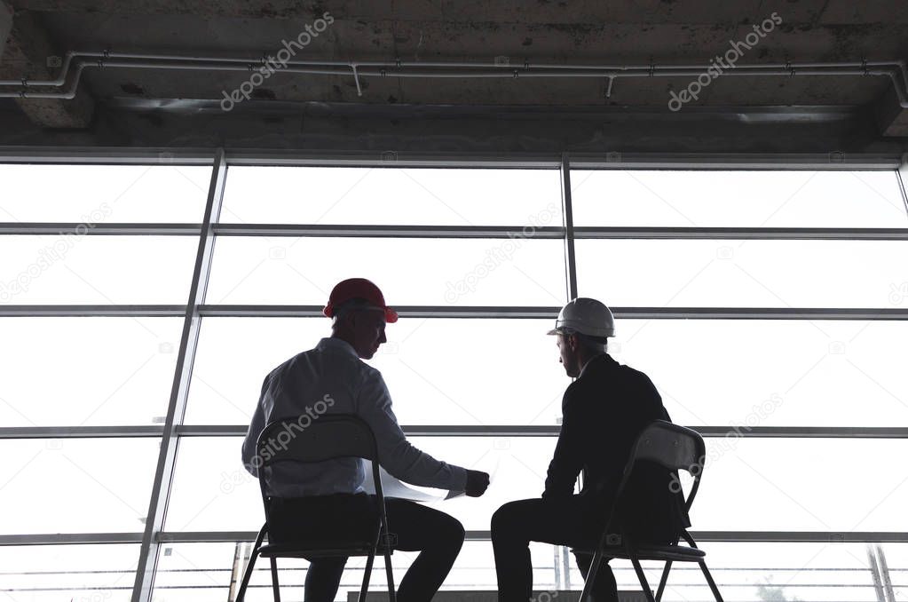 men engineers builders working at the table with a laptop, business negotiations at the construction site. silhouettes against the background of the window. bargain, apartment purchase, real estate