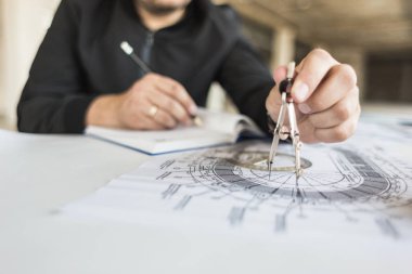 mimar builder çizimleri ile masada çalışıyor. Kask, çizimler, pergel işyerinde