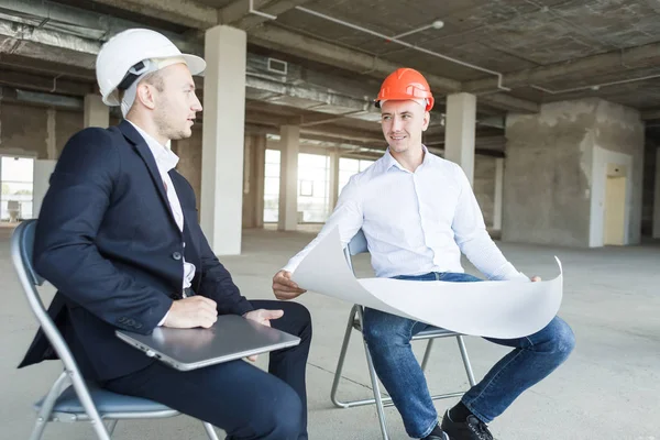 Hombres ingenieros constructores que trabajan en la mesa con un ordenador portátil, negociaciones comerciales en el sitio de construcción. ganga, compra de apartamento, bienes raíces — Foto de Stock