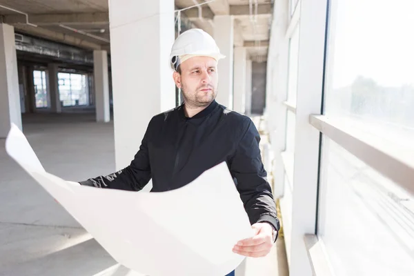 El arquitecto constructor en un casco con dibujos está trabajando en el sitio de construcción. supervisión de la construcción. ganga, compra de apartamento, bienes raíces — Foto de Stock