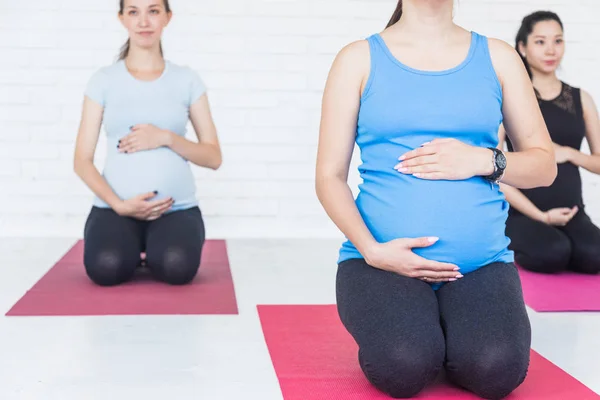 pregnancy, sport, fitness, people and healthy lifestyle concept - group of happy pregnant women exercising yoga and and meditating in lotus pose in white background gym