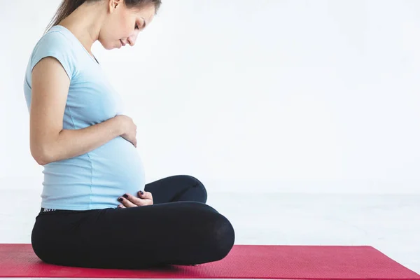 pregnancy, sport, fitness, people and healthy lifestyle concept - happy pregnant woman exercising yoga and and meditating in lotus pose in white background gym