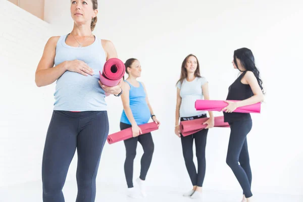 pregnancy, sport, fitness, people and healthy lifestyle concept - group of happy pregnant women exercising yoga and and meditating in lotus pose in white background gym