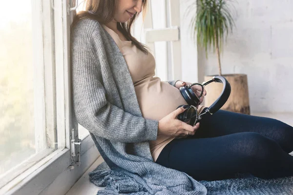 Junge schwangere Frau, die Musik hört und auf dem Sofa im Zimmer sitzt. klassische Musik für das Baby im Mutterleib — Stockfoto