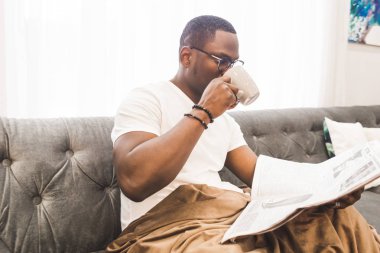 Genç Afrikalı-Amerikalı adam, evde gazete okurken bir battaniye ile örtülü.