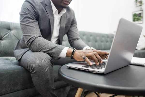 Joven hombre de negocios afroamericano en un traje gris que trabaja detrás de una computadora portátil . — Foto de Stock