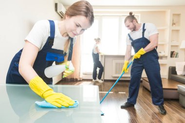 İş sırasında profesyonel ekipmanlarla temizlik hizmeti. Profesyonel mutfak temizliği, kanepe kuru temizleme, pencere ve yer silme. Erkek ve kadın üniformalı, tulumlu ve lastik eldivenli.