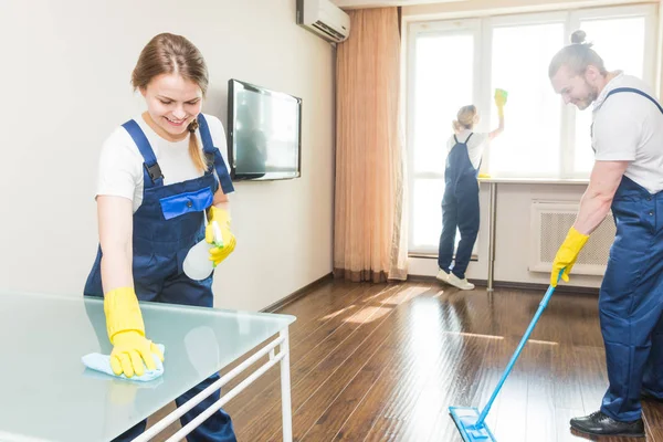 Layanan pembersihan dengan peralatan profesional selama bekerja. membersihkan dapur profesional, sofa dry cleaning, jendela dan pencucian lantai. pria dan wanita berseragam, semuanya dan sarung tangan karet — Stok Foto