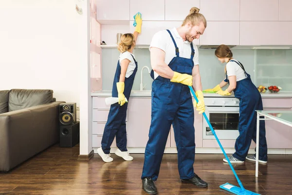 Serviço de limpeza com equipamento profissional durante o trabalho. limpeza kitchenette profissional, sofá limpeza a seco, janela e lavagem de piso. homem e mulher de uniforme, macacão e luvas de borracha — Fotografia de Stock