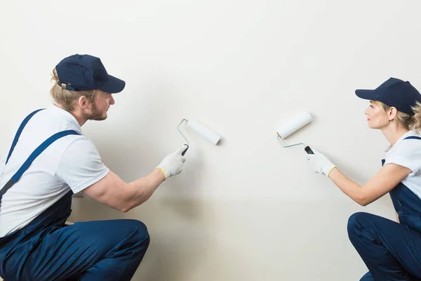 two worker professionally paint the walls of the room. people in uniform, in overalls and a cap with a roller and brush, apartment renovation, interior design, tinting. isolated