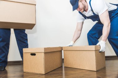 Delivery man loading cardboard boxes for moving to an apartment. professional worker of transportation, male loaders in overalls clipart