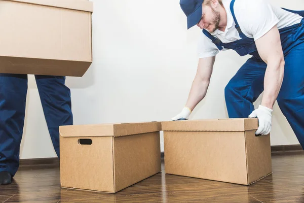 Entrega homem carregando caixas de papelão para se mudar para um apartamento. trabalhador profissional de transporte, carregadores masculinos em macacão — Fotografia de Stock