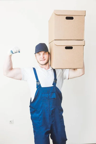Delivery strong, muscular man loading cardboard boxes for moving to an apartment. professional worker of transportation, male loaders in overalls. free space for text, isolated — Stock Photo, Image