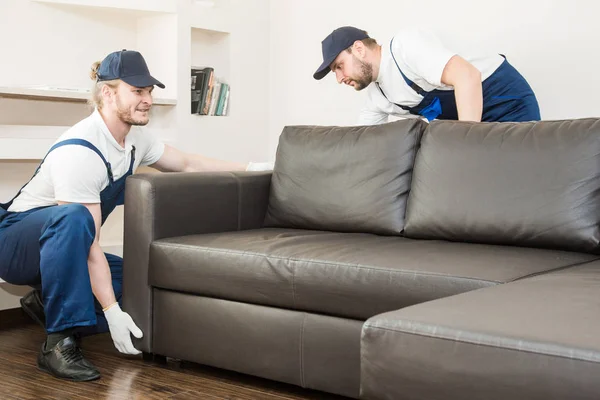 Entrega homem mover móveis transportar sofá para se mudar para um apartamento. trabalhador profissional de transporte, carregadores masculinos em macacão — Fotografia de Stock