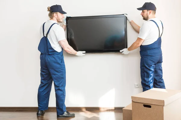 Entrega manremove a TV da parede para se mudar para um apartamento. trabalhador profissional de transporte, carregadores masculinos em macacão — Fotografia de Stock