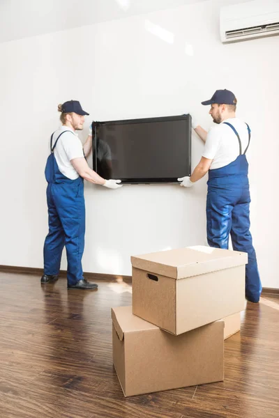 Entrega manremove a TV da parede para se mudar para um apartamento. trabalhador profissional de transporte, carregadores masculinos em macacão — Fotografia de Stock