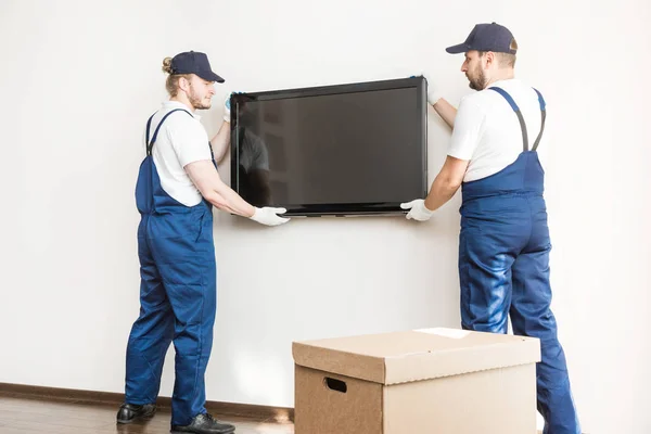 Entrega manremove a TV da parede para se mudar para um apartamento. trabalhador profissional de transporte, carregadores masculinos em macacão — Fotografia de Stock