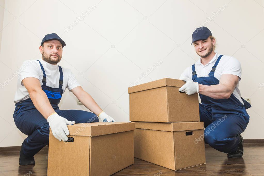 Delivery man loading cardboard boxes for moving to an apartment. professional worker of transportation, male loaders in overalls
