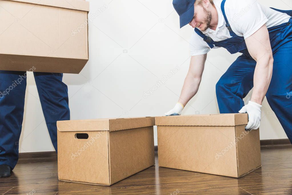 Delivery man loading cardboard boxes for moving to an apartment. professional worker of transportation, male loaders in overalls