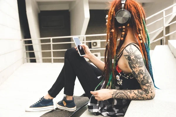 Молода дівчина з татуюванням і дредлоками слухає музику, сидячи на сходах — стокове фото