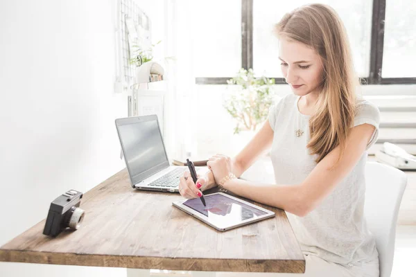 Νεαρή γυναίκα που εργάζεται στο σπίτι και ισοπαλίες στο tablet. Δημιουργική σκανδιναβικό στυλ χώρου εργασίας — Φωτογραφία Αρχείου