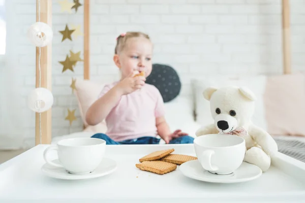 Cute little girl drinks tea with her teddy bear.