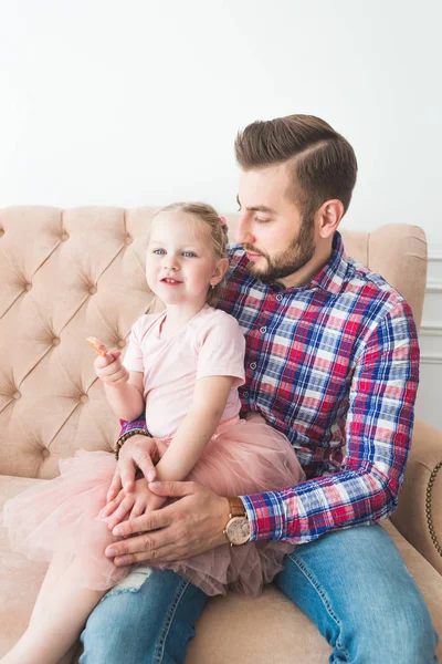 Linda niña con una piruleta sentada con papá en el sofá . — Foto de Stock