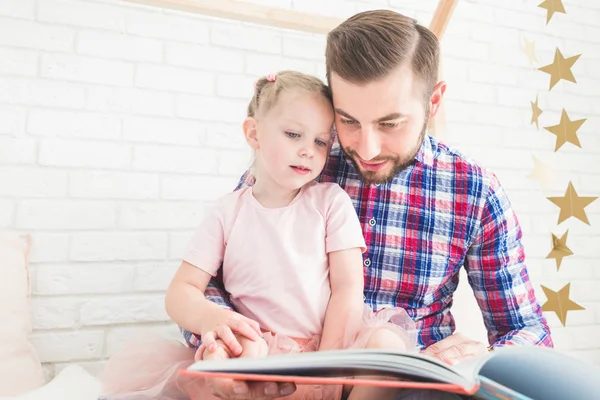 Dad and daughter sit together and read a book.